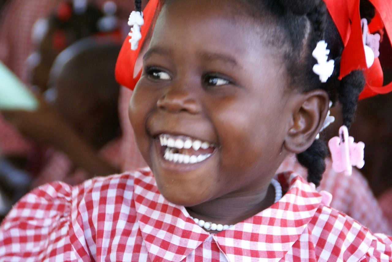 A smiling young child in a red-and-white school uniform, from the Haitian Children of Hope photo collection